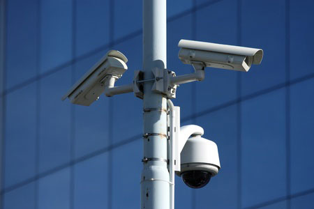 Obrazek przedstawia trzy kamery zabezpieczeń na słupie przed budynkiem